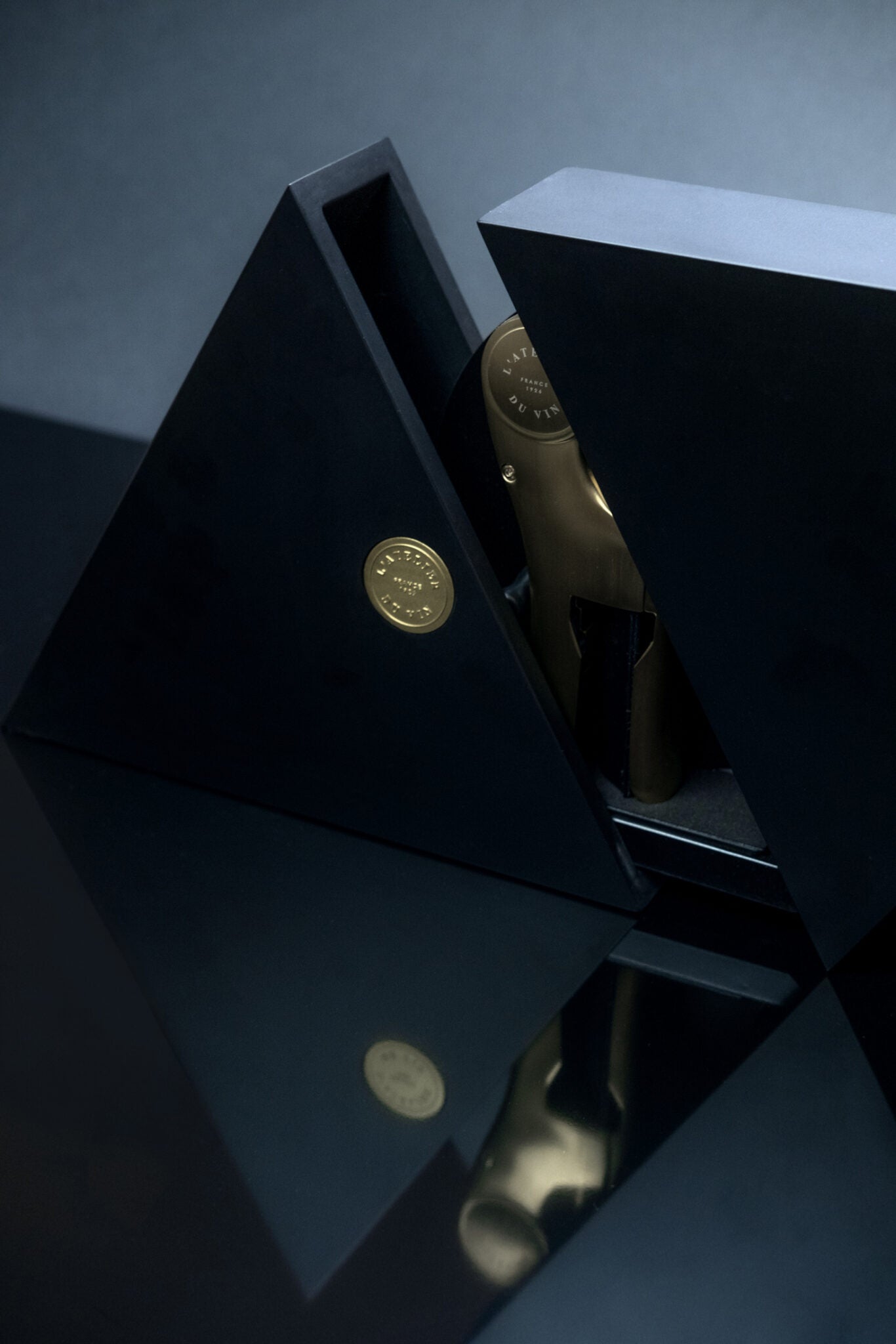 Detalle del estuche cerrado Geometry L'Atelier du Vin con sello dorado y reflejo sobre superficie oscura
