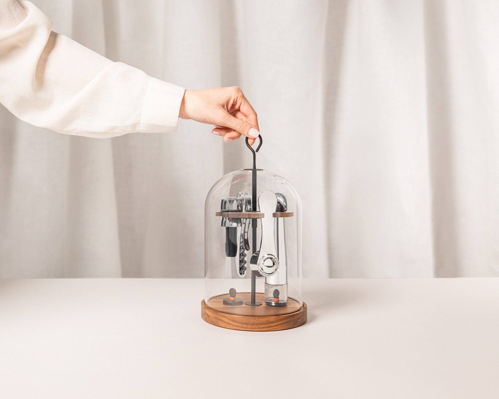 Mano levantando la campana de cristal del set L'Atelier du Vin Le Globe con accesorios en base de nogal