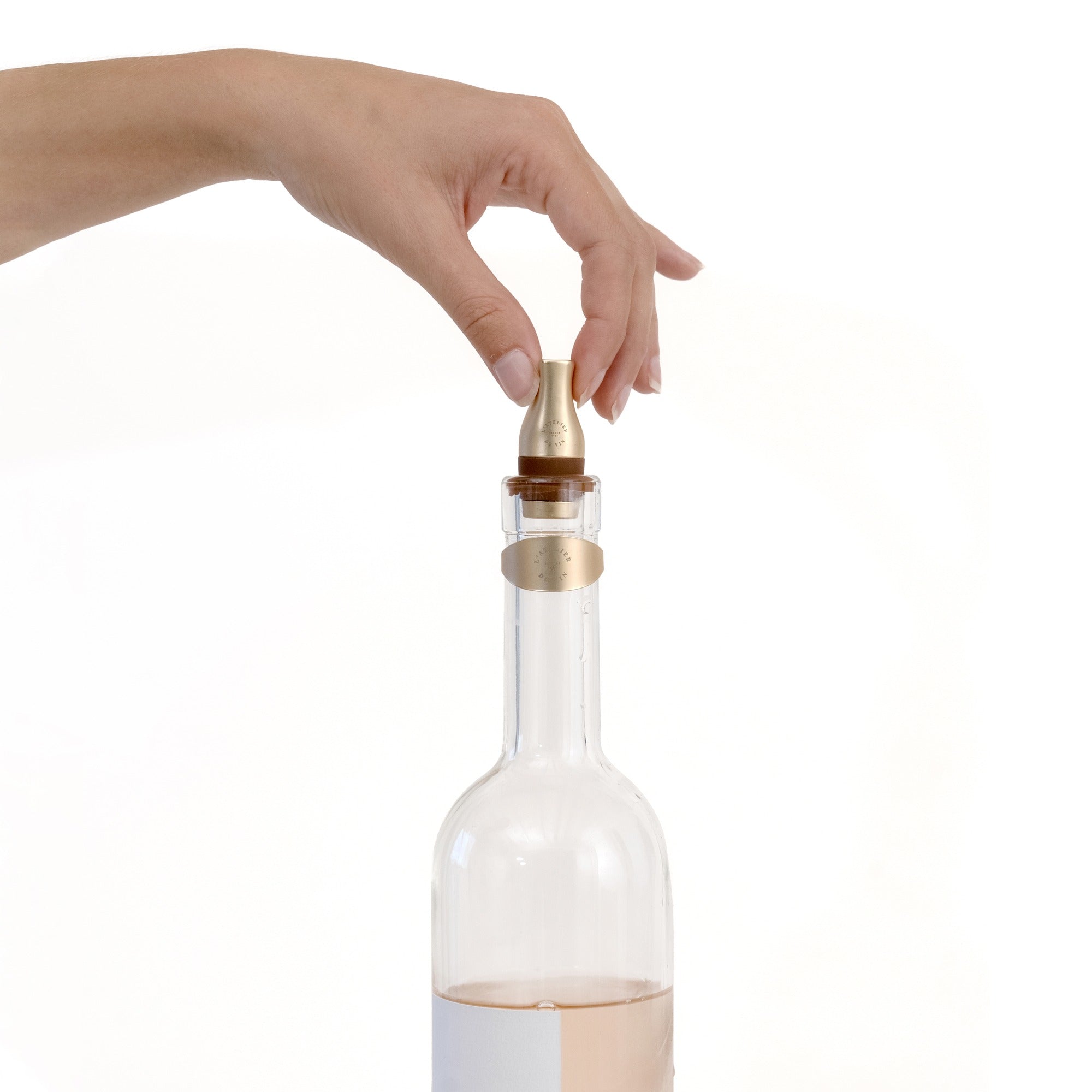 Mano colocando tapón Les Bijoux de L'Atelier du Vin en acabado dorado sobre botella de vino rosado