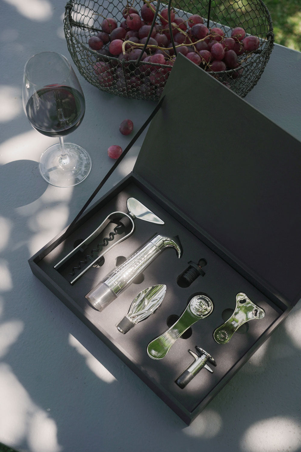 Caja L'Atelier du Vin Oeno Collection 2 abierta al sol con copa de vino tinto y uvas en exterior