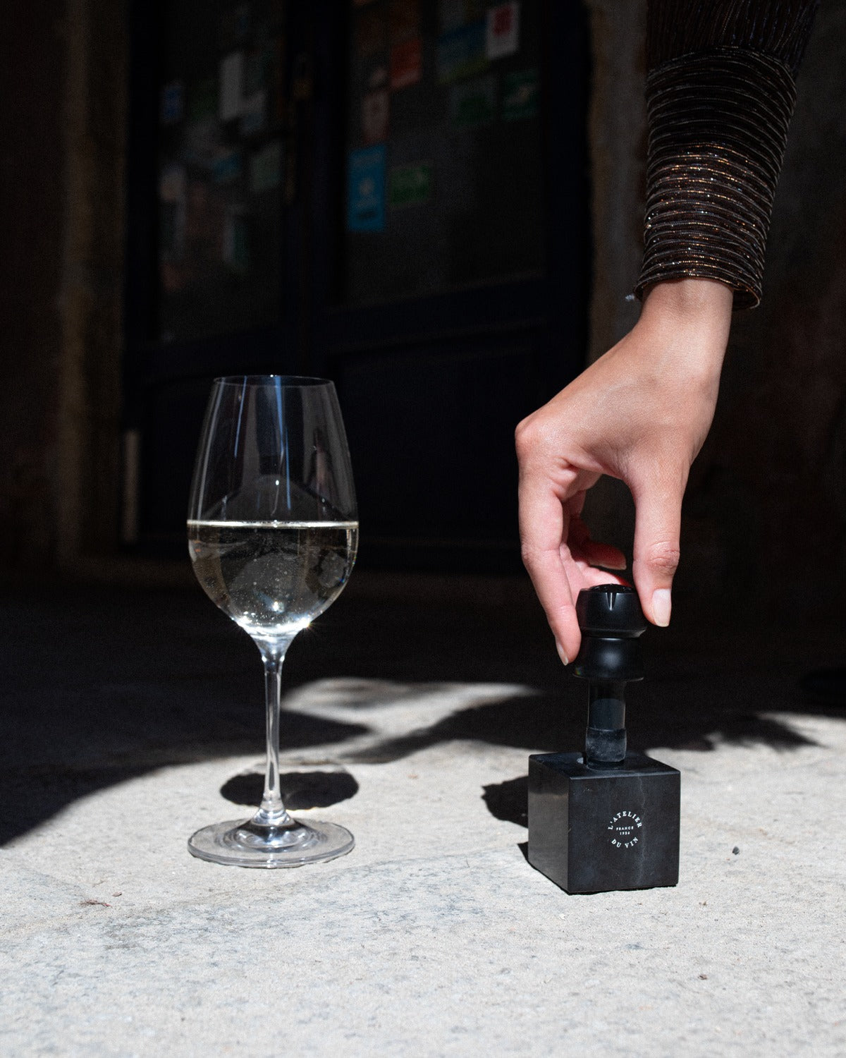 Mano tomando tapón L'Atelier du Vin Bubble Cork Black sobre cubo de mármol junto a copa de champán