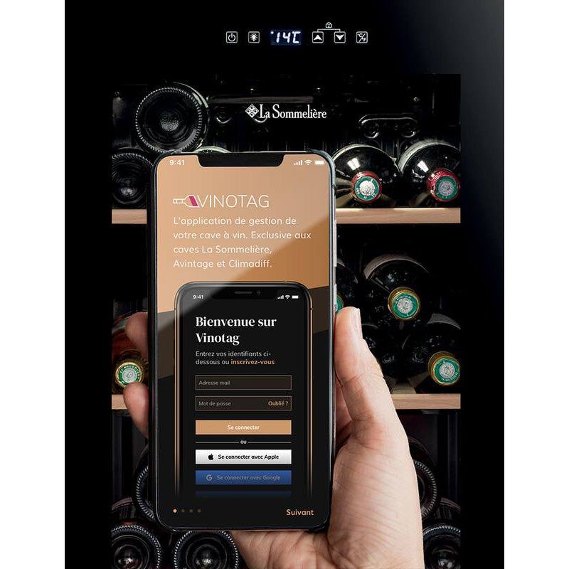 Mano sosteniendo un móvil con la app Vinotag frente a la vinoteca La Sommelière LS36 Black con botellas en su interior.