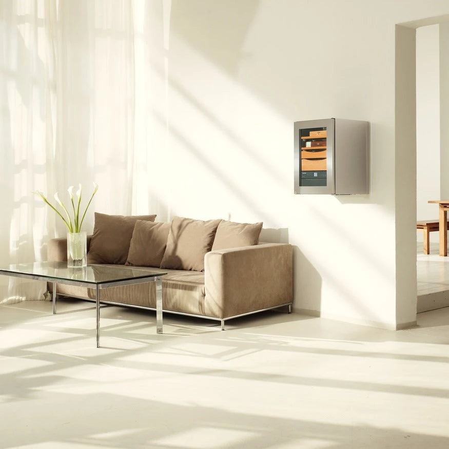 Cava de puros Liebherr ZKes 453 Humidor montada en la pared de una sala moderna y luminosa, con acabados metálicos y puertas de vidrio que dejan ver sus bandejas de madera para almacenar puros.