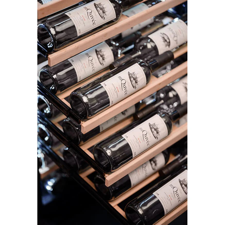 Primer plano inclinado de botellas de vino tinto mQuvée alineadas horizontalmente sobre estantes de madera en el interior de la vinoteca.