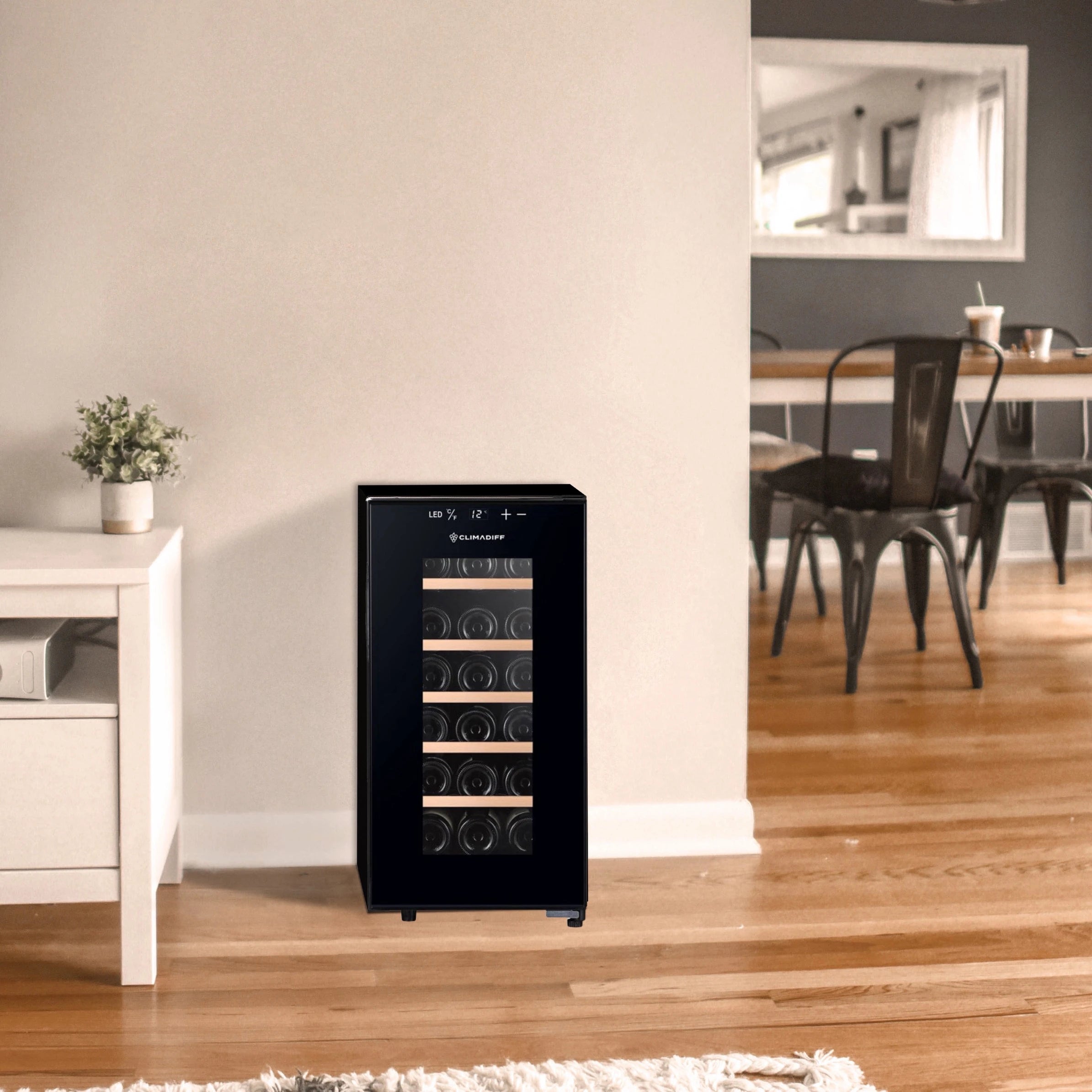 Vinoteca Climadiff CUVEE18 colocada junto a una pared en una sala moderna, parcialmente visible un comedor al fondo y un mueble blanco a la izquierda.