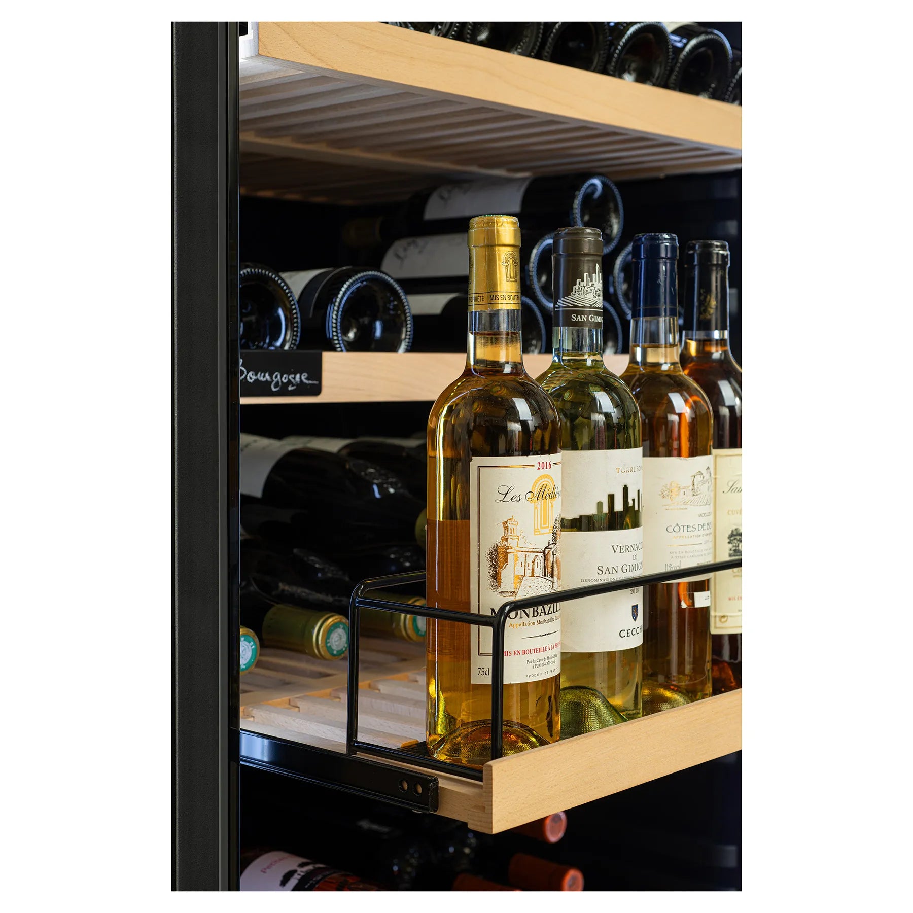 Botellas de vino blanco colocadas en posición vertical sobre una bandeja deslizante de madera con barandilla dentro de una vinoteca.