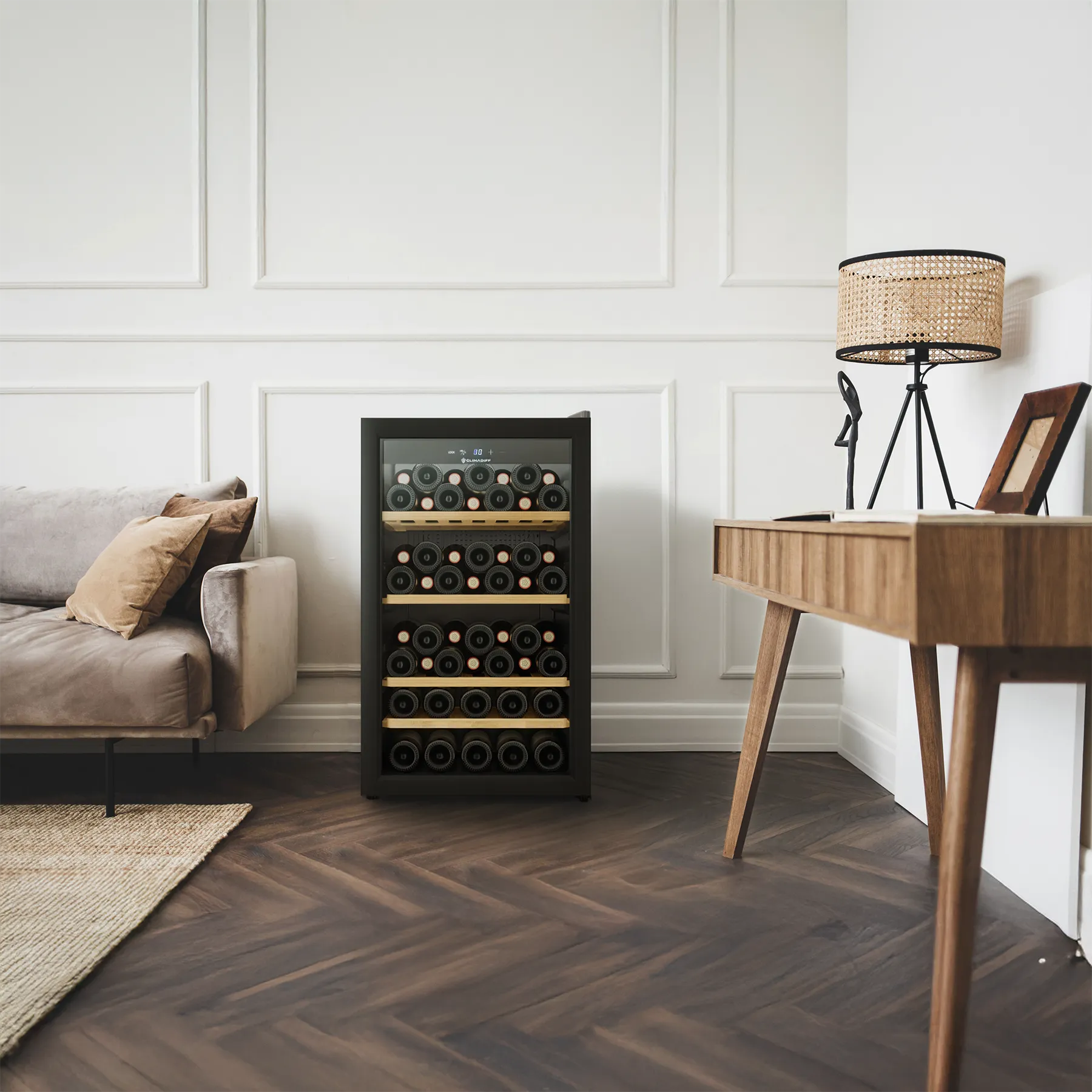 Vinoteca independiente Climadiff cls52b1 para 52 botellas, situada en una sala contemporánea con suelo de madera en espiga, sofá claro y escritorio de estilo moderno