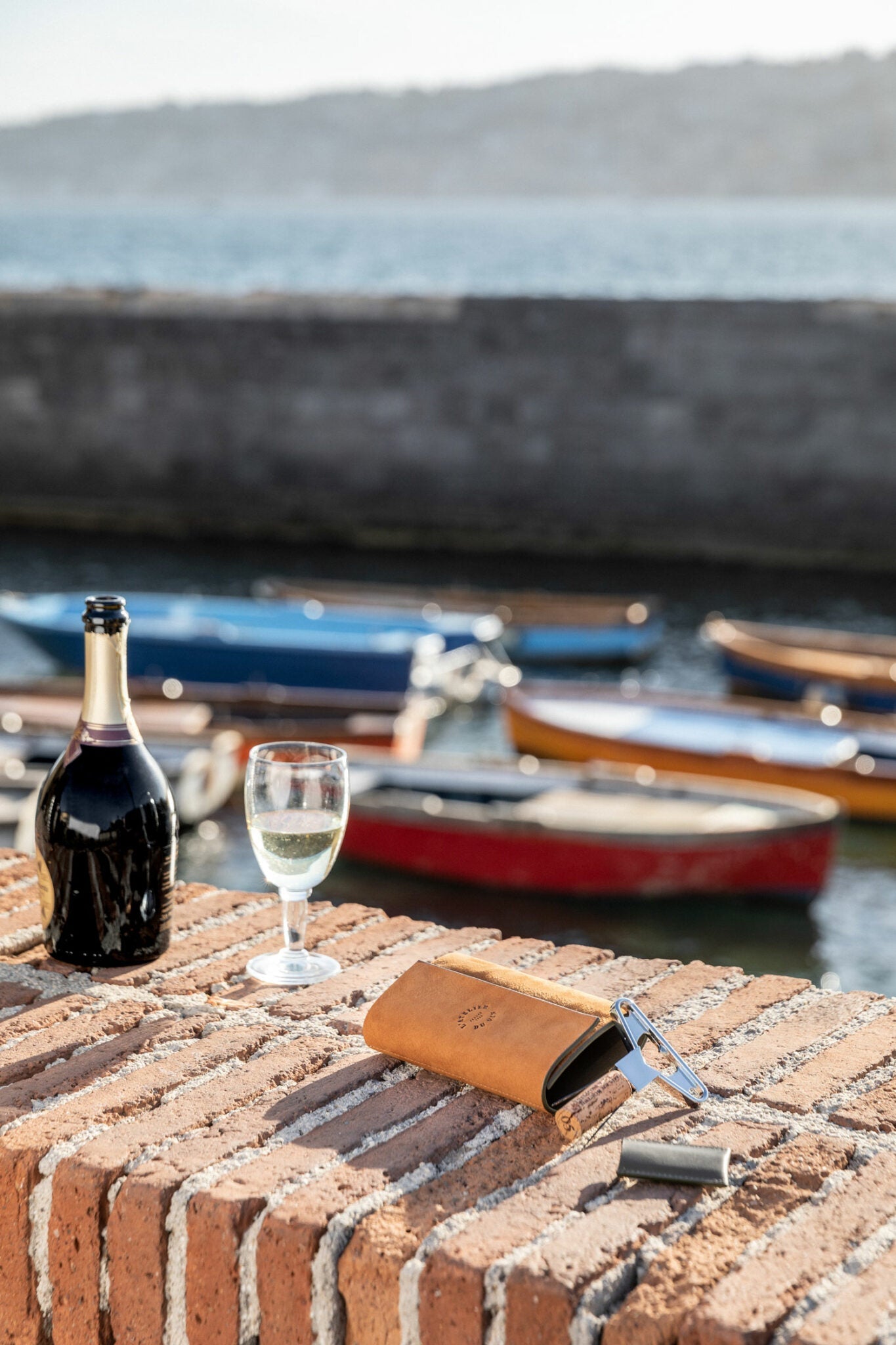 Estuche Bilame Nomad de L'Atelier du Vin abierto en muelle náutico con botella y copa de vino