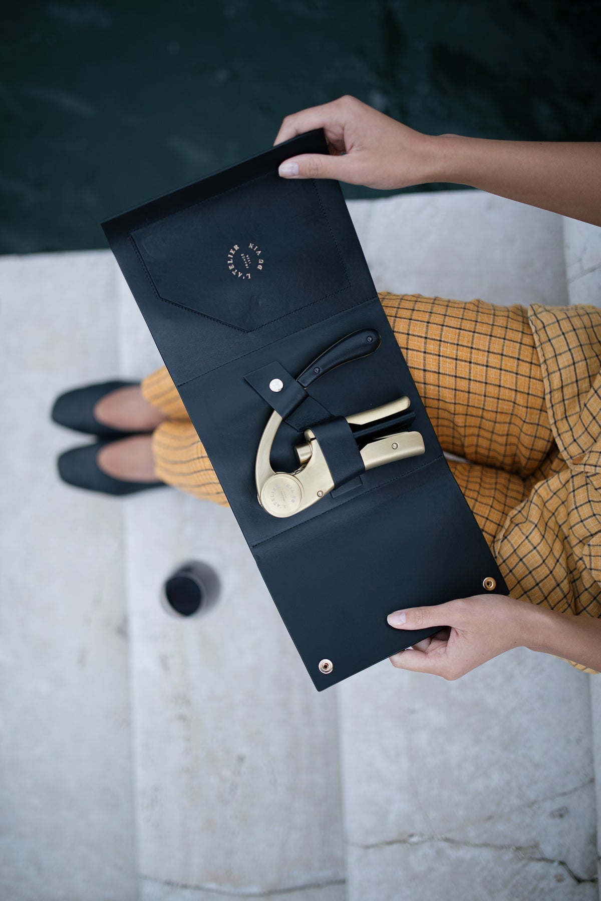 Manos abriendo el estuche de cuero negro Oeno Motion Gold Nomad L'Atelier du Vin en ambiente fashion