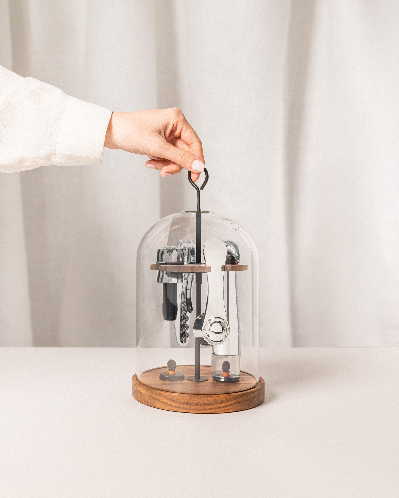 Mano levantando la campana de vidrio del set L'Atelier du Vin Le Globe para acceder a los accesorios