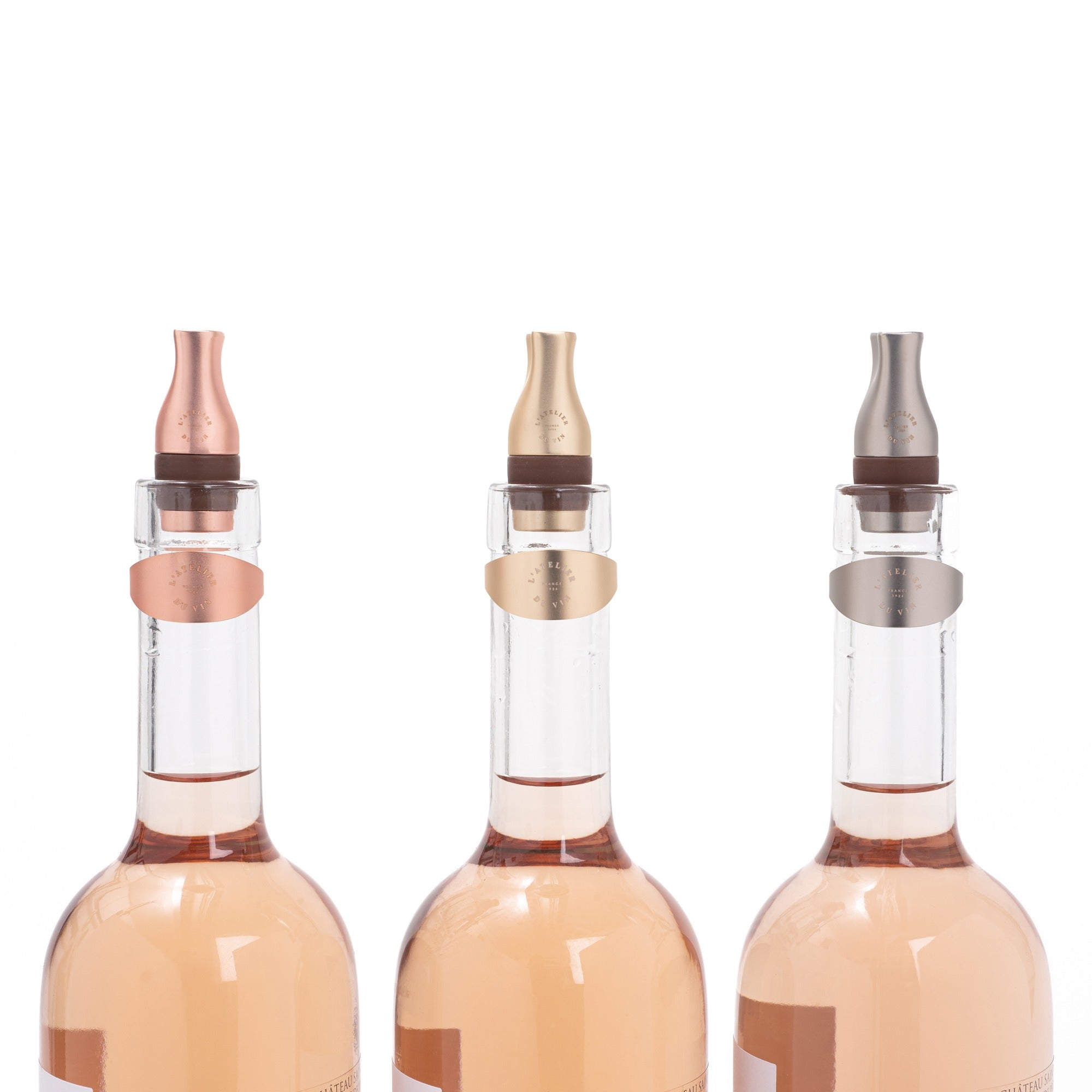 Tres tapones Les Bijoux de L'Atelier du Vin en acabados cobre, dorado y plata sobre botellas de vino rosado