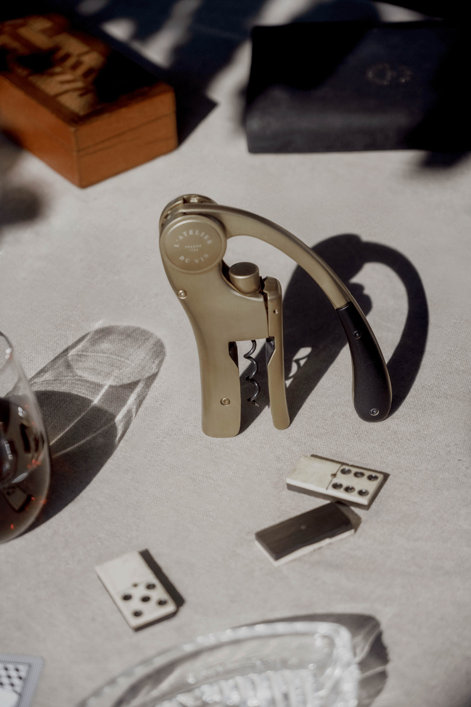 Sacacorchos dorado Oeno Motion Gold Nomad L'Atelier du Vin en ambiente nómada con naipes y copa de vino