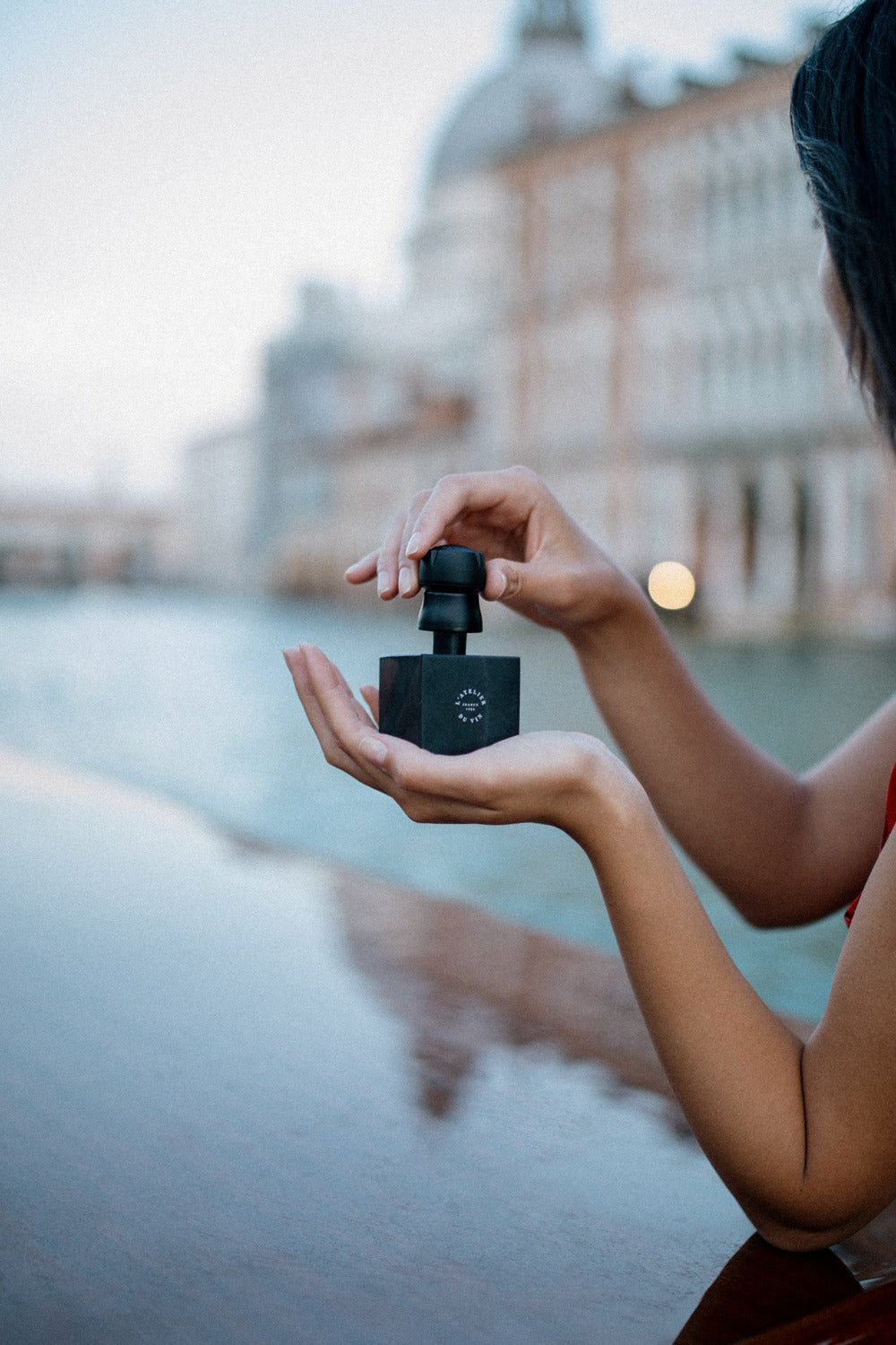 Mujer sosteniendo L'Atelier du Vin Bubble Cork Black frente a canal veneciano, imagen de estilo