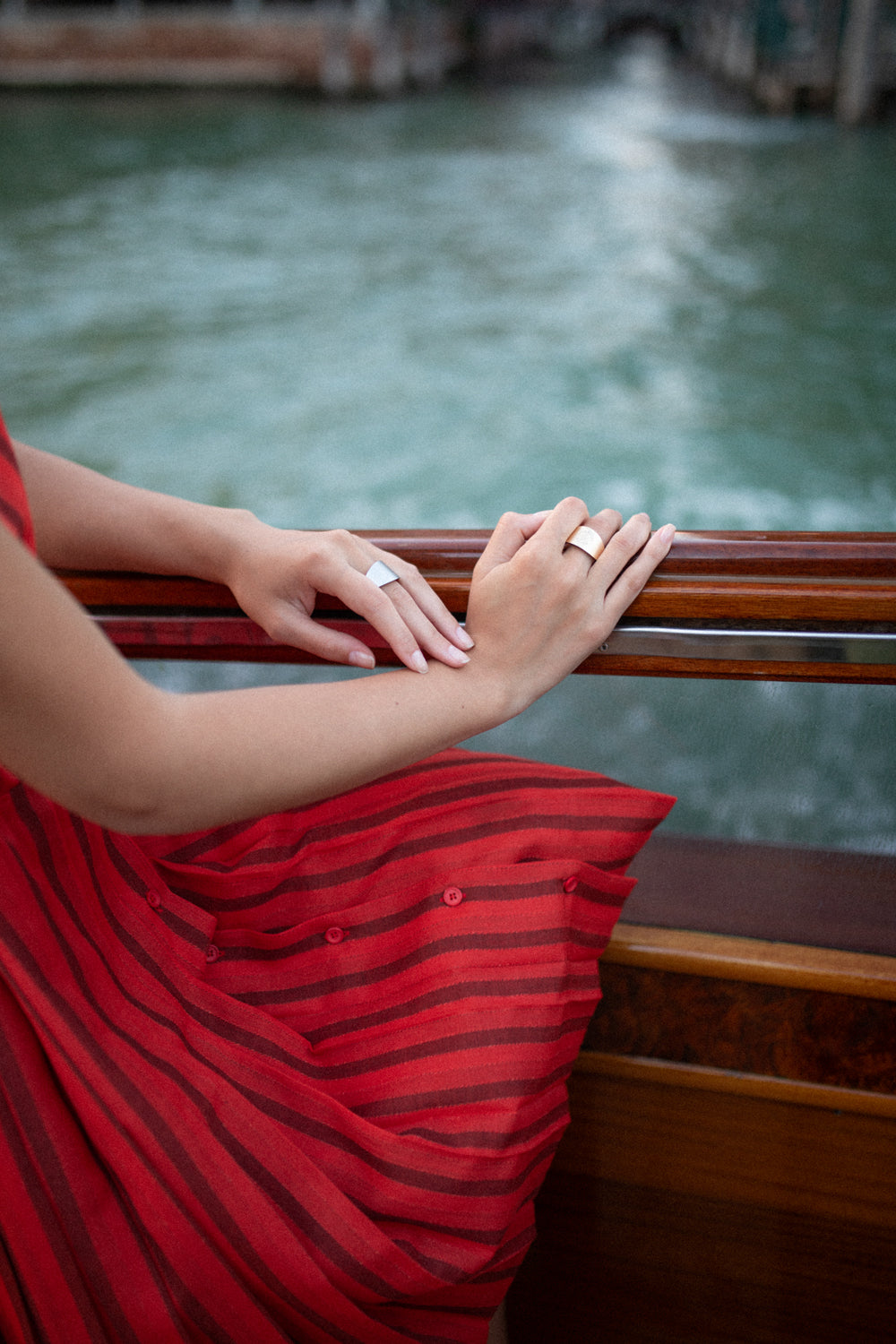 Manos con anillo plateado sobre barandilla de madera frente a canal de Venecia, imagen de estilo Les Bijoux