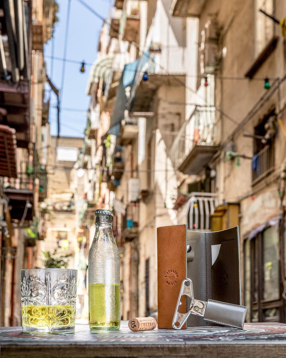 Estuche Bilame Nomad de L'Atelier du Vin en exterior urbano mediterráneo junto a copa y botella de vino