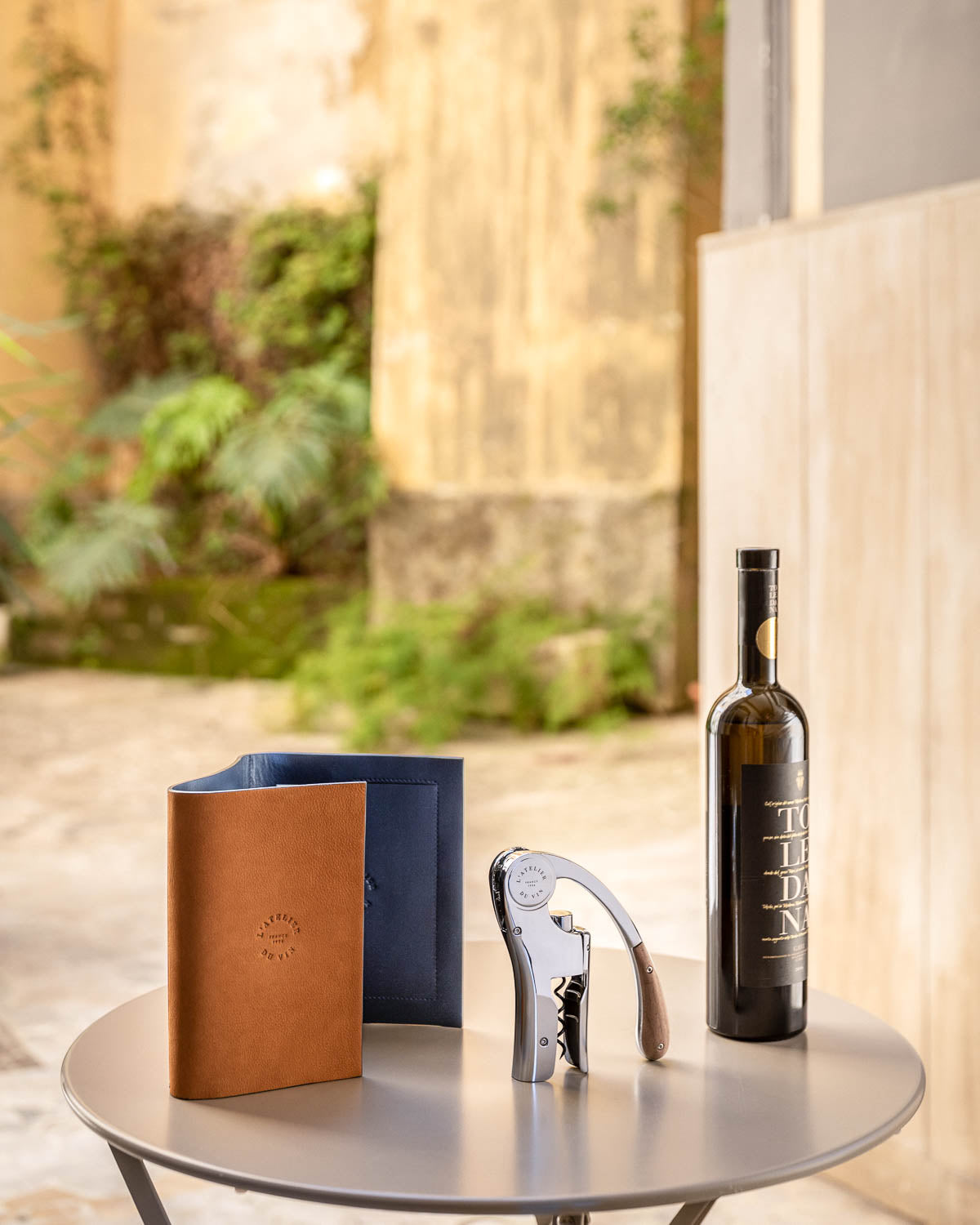 Estuche L'Atelier du Vin Oeno Motion Nomad con descorchador de palanca y botella de vino en terraza