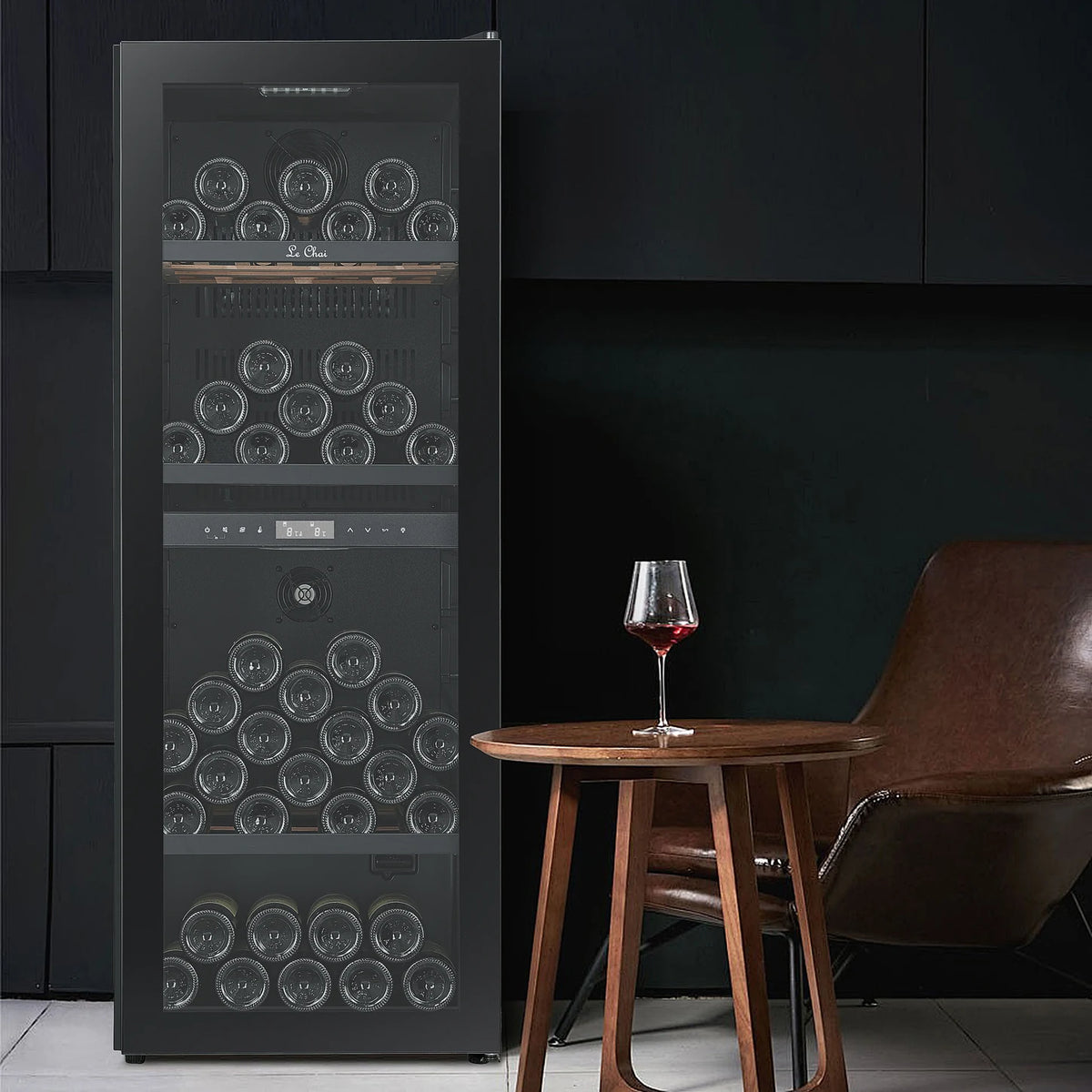 Vinoteca Le Chai LCT2FS100 de 100 botellas, en un salón junto a una mesa con una copa de vino tinto.