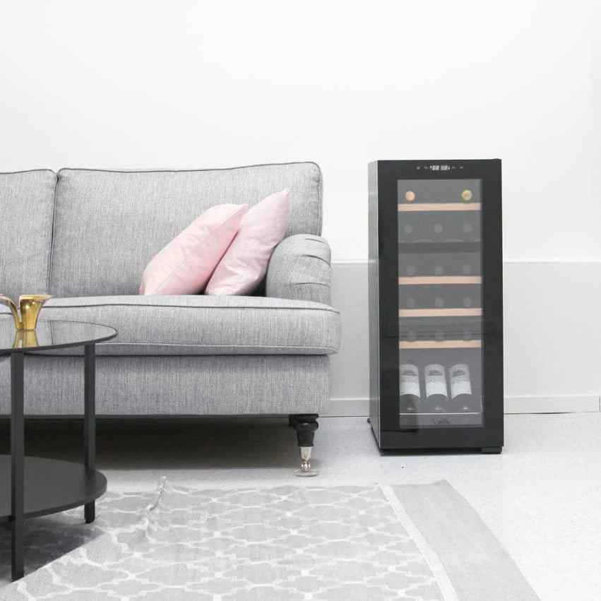 Vinoteca Cavin Northern Collection 18 Black con capacidad para 18 botellas, ubicada junto a un sofá gris con cojines rosados en una sala de estar minimalista.