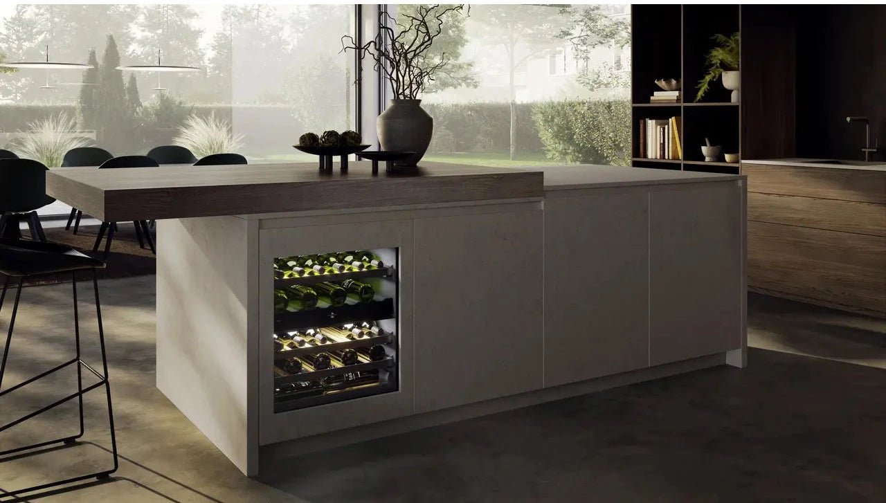 Cocina contemporánea con isla central que integra una vinoteca Liebherr UWpri 3662 iluminada, con botellas visibles en su interior y decoración minimalista sobre la encimera.