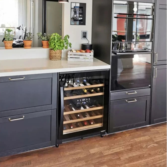 Vinoteca encastrable Cavin Scandinavian Collection 40 Fullglass Black, instalada bajo encimera en una cocina moderna; cuenta con estantes de madera y puerta de vidrio negro, con capacidad para 40 botellas de vino.